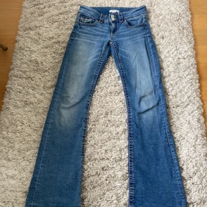 Blå bootcut jeans från Gina Tricot - Snygga blå jeans från Gina Tricot i klassisk bootcut-modell. Jeansen har ganska låg midja, fem fickor och dubbla silverfärgade knappar framtill. Tillverkade i slitstarkt denim.