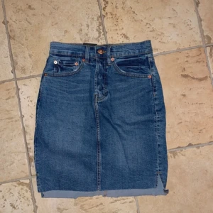 Mörkblå jeanskjol  - Snygg mörkblå jeanskjol från Lager 157. Kjolen har rå kant nertill, knapp- och dragkedjestängning samt två bakfickor. Perfekt för dig som gillar en enkel och tidlös stil.