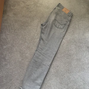 Grå loose fit jeans från Jack & Jones - Säljer ett par grå jeans från Jack & Jones i modellen Loose/Chris. Jeansen har en loose passform, raka ben och klassisk femficksdesign. Tillverkade i denim av bomull och har en snygg, tvättad grå färg som passar till det mesta. Stl 28/30
