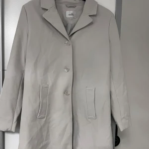 Kappa med knappar - Stilren kappa från Isolde med klassisk krage och tre knappar framtill. Jackan har två fickor och är helfodrad för extra komfort. Perfekt för dig som gillar en enkel och clean look.