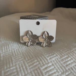 Silvriga blomformade örhängen - Snygga örhängen i silverfärgat material med blommig form och detaljerade blad. Perfekta för att ge din look en fräsch och trendig touch. Blommönstret gör dem unika och stilrena.