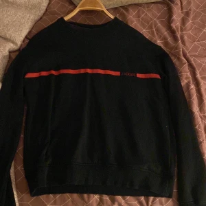 Svart sweatshirt från NA-KD med röd detalj - Svart sweatshirt från NA-KD i storlek L med en röd horisontell linje och texten 'J'ADORE' framtill. Tröjan har rund halsringning och långa ärmar, perfekt för en chill och stilren look.