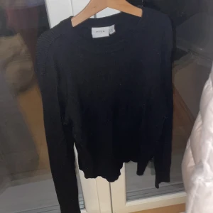 Svart stickad tröja från Vila - En svart stickad tröja från Vila med rund halsringning och ribbade detaljer vid axlar och hals. Tröjan har lång ärm och en klassisk, enkel design som är lätt att matcha med allt. Perfekt för lager-på-lager under kyliga dagar.
