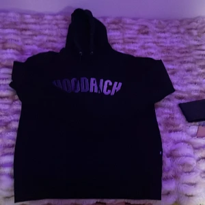 Svart hoodie från Hoodrich - Svart hoodie från Hoodrich med stor logga i vitt över bröstet. Klassisk modell med huva och dragsko, samt långa ärmar. Perfekt för dig som gillar streetwear och vill ha en stilren look.