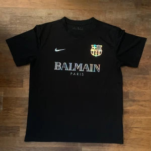 Svart FC Barcelona x Balmain tröja Nike M - Snygg svart fotbollströja från Nike i samarbete med FC Barcelona och Balmain Paris. Tröjan har holografiska detaljer på logga, Nike swoosh och text. Tillverkad i lätt och ventilerande material, perfekt för dig som vill sticka ut på planen eller gatan.