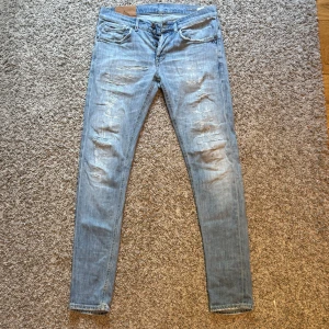 Dondup George Jeans (Ljusblå) - Snygga dondup jeans som säljes. Jeansen har lagats ett flertal gånger då alla slitningar inte är orginal.(Se bild 5, reperationer). Däremot inget jag tycker har sänkt utseendet av plagget. En fläck, (Se vild 4) som förekom när jag använde textil lim. Passar nog dig som väger runt 70 kilo och är cirka 180cm. Pris kan diskuteras