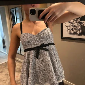 Topp - Supersöt blus i svartvitt mönster med svarta axelband och en dekorativ svart rosett under bysten. Storlek L men passar absolut S/ M. Använd 1 gång!