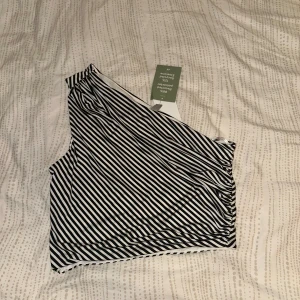 Randig one shoulder topp från H&M - Snygg svartvit randig topp från H&M med one shoulder-design. Helt oanvänd och etiketten finns kvar på!