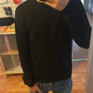 Svart stickad tröja från Lindex - En svart, enkel och stilren stickad tröja från Lindex. Tröjan har rund halsringning och långa ärmar, perfekt att matcha med jeans. Mjuk och skön, passar dig som gillar en klassisk look. Måste handtvättas.