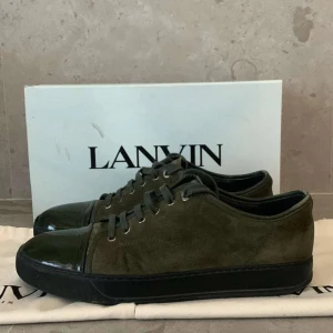 Gröna sneakers från Lanvin - Säljer ett par snygga gröna sneakers från Lanvin i bra skick, lite defekt och slitning på cap toe. Skorna har en stilren design med snörning och en glansig tå i skinn. Perfekta för både vardag och fest! Kommer med originalförpackning och dustbag.