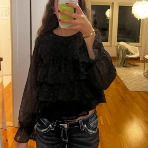 Blus med volanger från Gina Tricot - Supersöt svart blus med långärmar, volanger och har dessutom en söt knäppning där bak. Använt endast en gång! Passar perfekt till jul eller nyår! Pris går att diskutera💞
