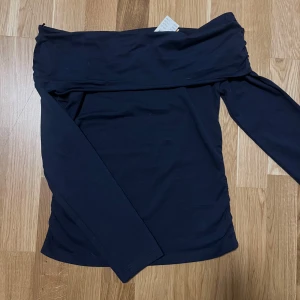 Shoulder off top - Längärmad off shoulder topp med rynkningar i sidorna. Toppen är marinbla och har nervikt ovankant. Det stảr storlek 170 men jag skulle säga att det passar S