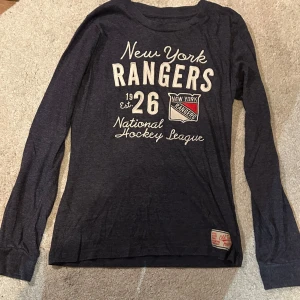 Blå långärmad New York Rangers-tröja - Snygg mörkblå långärmad tröja från Old Time Hockey med New York Rangers brodyr och tryck framtill. Tröjan har rund halsringning och är tillverkad i mjuk bomullsmix. Perfekt för en dag när man vill ha något bekvämt och snyggt. Står ingen storlek men skulle säga att den passar som S (Stretchigt tyg dock så passar någon med större storlek också)