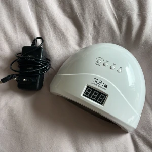 SUN 1S UV/LED Nail Lamp - SUN 1S UV/LED nagellampa med digital display och timerfunktioner (10s, 30s, 60s, 99s low heat mode). Levereras med strömadapter. Lampan är i gott skick med mindre spår av användning invändigt. Perfekt för gel- och shellacmanikyr hemma.