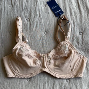 Oanvänd Beige spets-bh från Fantasie Jocelyn - Säljer en beige bh från Fantasie, modell Jocelyn, i storlek 65D. Bh:n har vackra spetsdetaljer upptill, broderade mönster och justerbara axelband. Kuporna är lätt mönstrade och bh:n stängs med hysk- och hakknäppning bak. Skulle säga att den är en storlek mindre i kupan🫶🏻