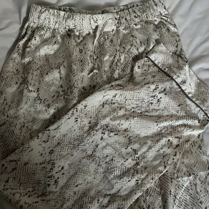 Satinbyxor med ormmönster och snörning - Snygga byxor i glansigt satinmaterial med beige och brunt ormmönster. De har elastisk midja med snörning och avslappnad passform. Perfekta för dig som vill sticka ut med ett coolt mönster och skön känsla.