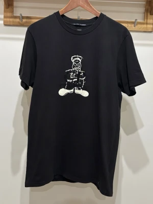 C.P. Company svart T-Shirt - Svart t-shirt från C.P. Company med en stor broderad grafisk figur på bröstet i vitt. Klassisk rund hals och korta ärmar. Perfekt för dig som gillar streetwear och vill sticka ut med en unik detalj på din outfit.