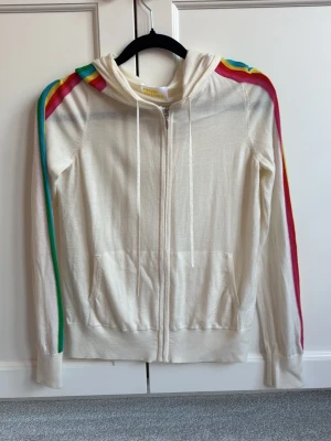 Vit hoodie From Future - Snygg vit hoodie från From Future med dragkedja och huva. Långa ärmar med färgglada regnbågsränder längs axlar och armar. 