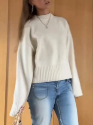 Vit stickad tröja med breda ärmar - Säljer en stilren vit stickad tröja med bred ribbad mudd i nederkant och vid ärmslut. Tröjan har en rak passform och något bredare ärmar för en trendig look. Perfekt att matcha med jeans för en enkel men snygg outfit.