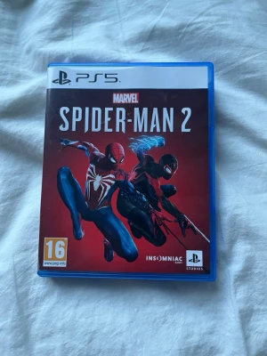 Marvel's Spider-Man 2 till PS5 - Säljer Marvel's Spider-Man 2 till PlayStation 5. Spelet kommer i ett blått plastfodral med snyggt omslag där både Peter Parker och Miles Morales syns. Skivan har en svartvit spindel-logga. Perfekt för dig som gillar action och superhjältar! Och aldrig använt skivan så den är helt sprillans ny 