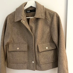 Zara jacka - Kort jacka från Zara, nästan aldrig använd. Jackan har guldiga tryckknappar och är tillverkad i ullblandning. Står strl S i den men är mer som en XS