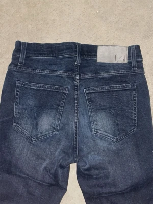 Svarta slim fit jeans från Tiger of sweden - Snygga svarta slim fit jeans från Tiger of sweden med klassiska fem fickor. Jeansen har en stilren look med svarta sömmar och patch med logga bak i midjan. Perfekta för en trendig och avslappnad stil. Storlek W29 L32