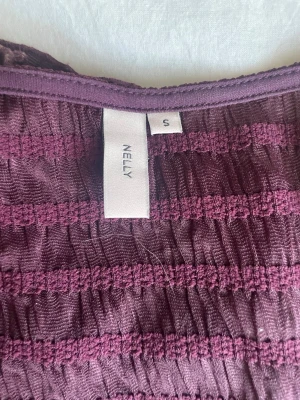  topp från Nelly - Supersnygg röd topp från Nelly med lång ärm och smockad struktur. Toppen har en figurnära passform och en lätt v-ringad halsringning. Perfekt att styla med jeans eller kjol för en trendig look.