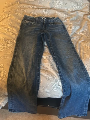 Blå raka jeans med broderad ficka - Säljer ett par blå jeans med rak passform och snyggt broderi på bakfickan. Jeansen har klassisk femficksdesign, normal midja och är tillverkade i denim. Perfekta för dig som gillar en avslappnad men ändå trendig look.