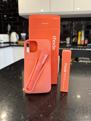 Rhode skal och lipptint - 🎨 Färg: peachy pit 📱 Passar: iPhone 13 / 14 / 15 (ej pro, max eller plus) ♻️ Skick: Helt ny – aldrig använd 📦 Skickas samma dag vid köp