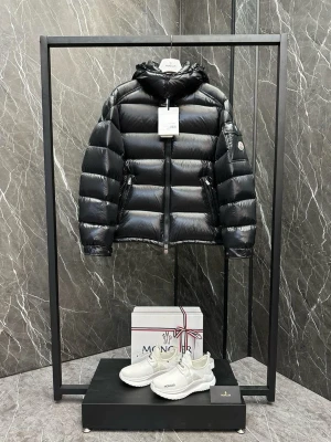 Svart dunjacka från Moncler - Snygg svart dunjacka från Moncler med glansig finish och puffig design. Jackan har huva, dragkedja framtill, två sidofickor med dragkedja och Moncler-logga på ärmen. Perfekt för kalla vinterdagar och riktigt trendig look.