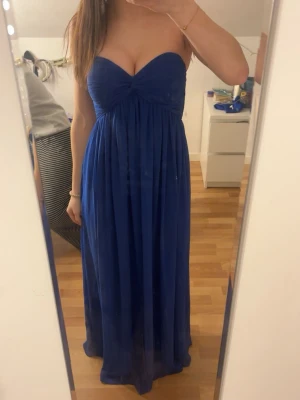 Bal/fest klänning  - Säljer en marinblå axelbandslös långklänning från NLY Trend i storlek 36. Klänningen har en snygg v-ringad överdel med twistad detalj framtill och ett luftigt, fallande tyg. Funkar både som bal klänning eller bara en lite finare klänning!!