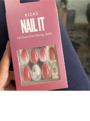 KICKS Nail It Cherry Press-on naglar - 24-pack press-on naglar i mandelform från KICKS. Naglarna har en rosa bas med vit ombre och några dekorerade med söta körsbärs- och blommotiv. Perfekt för dig som vill ha en söt och trendig look utan att gå till salong.