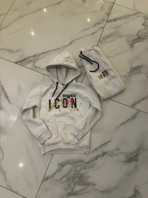 Dsquared2 ICON tracksuit – hoodie & byxor  - 🔥 Dsquared2 ICON tracksuit – hoodie & byxor 🔥  Snygg och exklusiv tracksuit från Dsquared2 ICON i vitt med färgstarkt tryck. Setet består av hoodie och matchande byxor och är i fint skick. Stilren men samtidigt trendig design som verkligen sticker ut – perfekt för både vardag och coola outfits.  Storlek 146–152, sitter bekvämt och är skön i materialet. Nypris är betydligt högre än annonspriset.  💰 Pris: 749 kr 💬 Pris kan diskuteras vid snabb affär. ⏳ Först till kvarn!  Hör gärna av dig vid frågo