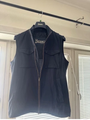 Herno/ Loro Piana  - Stilren mörkblå väst från Herno med dragkedja framtill och fyra fickor, två på bröstet och två vid sidorna. Västen har en klassisk krage och är perfekt för lager-på-lager. Enkel och snygg design som passar till mycket.