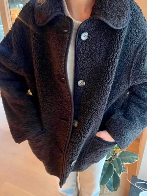 Svart teddyjacka med stora knappar - Mysig svart teddyjacka med stora knappar framtill och klassisk krage från Urban Outfitters. Jackan har två sidofickor och är tillverkad i ett fluffigt, mjukt material som håller dig precis lagom varm🌼💗 Perfekt teddyjacka på våren och hösten för en trendig look. Den funkar till och med som vinterjacka med en varm tröja under🥰 Storlek S/M och toppen skick. Ursprungspris 1000kr. Säljer för 550kr😱