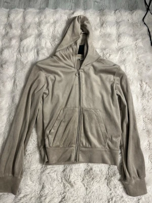 Beige velourhoodie med dragkedja - Säljer en beige hoodie i mjuk velour från lager 157. Hoodien har dragkedja framtill, kängurufickor och en klassisk huva. Perfekt för en chill och avslappnad stil. Materialet är lent och ger en lyxig känsla.