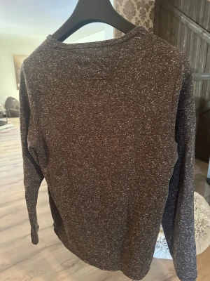 Tiger of Sweden Mörkgrå melerad långärmad tröja - Mysig långärmad tröja från Tiger of Sweden i mörkgråmelerat tyg. Tröjan har rund halsringning och en enkel, stilren design som passar perfekt till jeans eller chinos. Materialet är mjukt och bekvämt, perfekt för kyligare dagar.