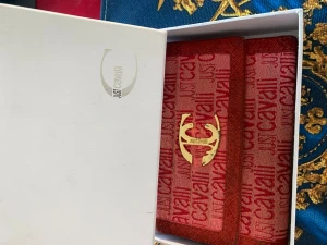 Röd plånbok från Just Cavalli - Snygg röd plånbok från Just Cavalli med logotyp i guld framtill. Plånboken har ett mönster med Just Cavalli-tryck över hela ytan och är tillverkad i textilmaterial med detaljer i äkta läder. Kommer i original ask.