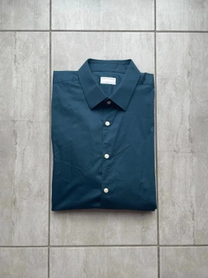 Mörkblå skjorta från Tiger of Sweden  - Stilren mörkblå skjorta från Tiger of Sweden med klassisk krage och vita knappar. Skjortan är långärmad och tillverkad i mjuk bomull, perfekt för en clean och enkel look. Vid frågor eller funderingar skriv gärna!