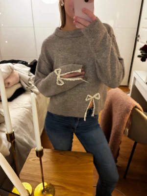 Grå stickad tröja med spetsrosetter - Super gullig stickad tröja med spets rosetter som detaljer. Tröjan är från barnavdelningen på Zara i storlek 164 men passar som en xs. (Jag är 160 och den sitter bra på mig). Knappast använd!!🤎🤎