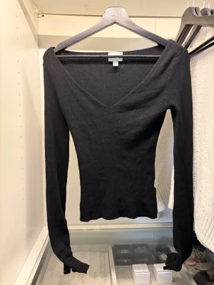 Svart ribbad långärmad topp V-ringad - Säljer en svart ribbad långärmad topp från H&M med snygg V-ringning. Modellen är slim och sitter tajt mot kroppen, perfekt för dig som gillar en enkel men stilren look. Materialet är mjukt och stretchigt, vilket gör den skön att bära hela dagen. 