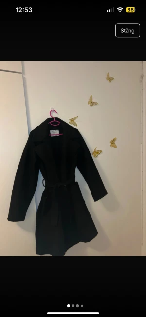 Svart kappa med bälte från KappAhl - Snygg svart kappa från Amisu med bred krage och knytbälte i midjan. Jackan har långa ärmar och två stora fickor framtill. Perfekt för dig som gillar klassisk stil med en modern touch.