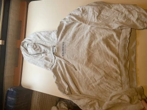 Grå hoodie Calabasas XL - Snygg grå hoodie från Calabasas i storlek XL med tryck både fram och bak. Mjuk insida i fleece och klassisk huva med dragsko. Texten på ryggen har Los Angeles, California och årtal. Perfekt för chill dagar och streetwear-stil.