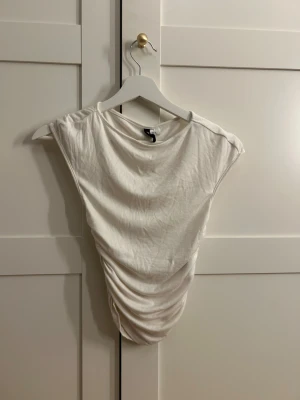 Vit omlott linnetopp från Divided XS - Säljer en vit linnetopp från HM i storlek XS. Toppen har omlott-effekt med snygga draperingar framtill och är ärmlös med rund hals. Perfekt för dig som gillar stilrena och enkla plagg med en twist. Materialet är mjukt och skönt bomull.