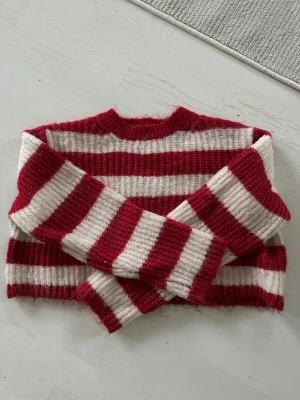 Randig röd och vit stickad tröja Bershka - Säljer en mysig stickad tröja från Bershka med breda röda och vita ränder. Tröjan har lång ärm, ribbad struktur och en croppad passform som ger en cool vibe. Perfekt för dig som gillar att sticka ut med färg och mönster.