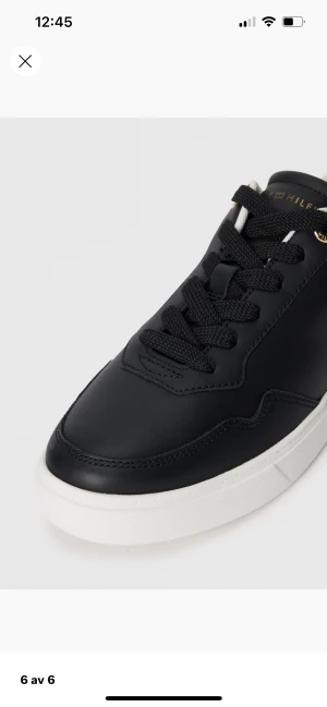 Svarta sneakers från Tommy Hilfiger - Snygga svarta sneakers från Tommy Hilfiger med vit platt sula och gulddetaljer. Skorna har rund tå, snörning och är tillverkade i skinn. Diskret TH-logo i guld på sidan och vit hälkappa med guldfärgad detalj. Perfekta för dig som gillar stilrena och klassiska sneakers. Ovända !! Jag köpte de för 1300 kr säljer för 1000 . 