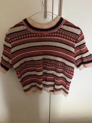 Randig stickad tröja från InWear - Säljer en kortärmad stickad tröja från InWear i storlek S. Tröjan har ett randigt mönster i beige, svart, rött och orange 