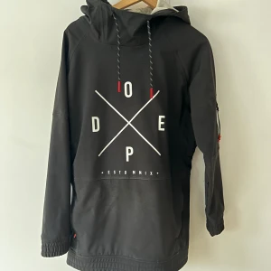 Svart vindjacka från Dope - Svart vindjacka från Dope med stor vit grafisk print på framsidan och coola röda detaljer på snörningen. Jackan har huva, långa ärmar och elastiska muddar. Storleken är small men passar även mig som är en m