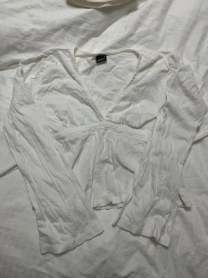 Vit omlottblus från Gina Tricot - Säljer en vit omlottblus från Gina Tricot i storlek S. Blusen har långa ärmar, v-ringad hals och ett snyggt knyt i midjad! Den är lite skrynklig eftersom den varit vikt länge😅🩷🩷