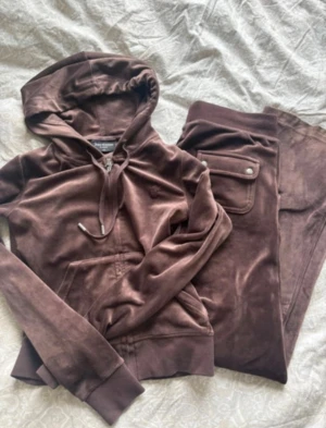 Bruna mjukisbyxor juicy couture sett - Säljer ett par bruna mjukisbyxor från Juicy Couture i mjuk velour. Byxorna har resår i midjan och muddar vid bensluten samt en ficka med lock och knapp bak. Perfekta för en chill och avslappnad look.
